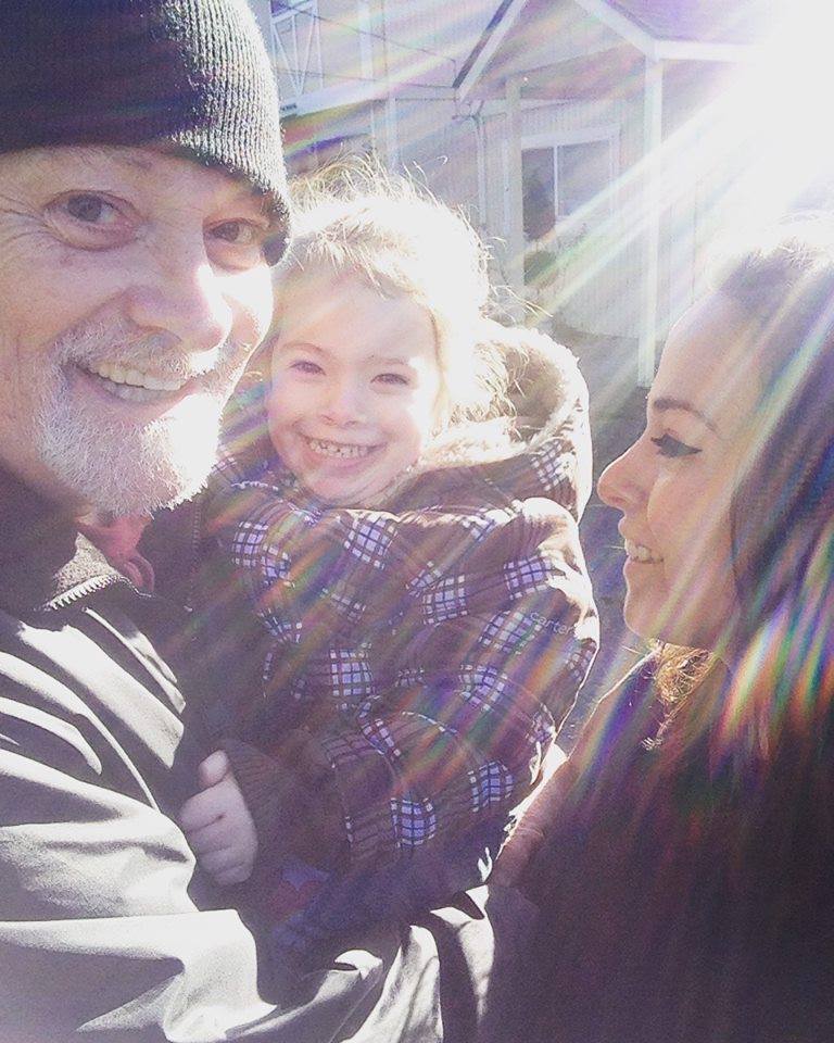 Richard holding a child with sunlight streaming through the trees